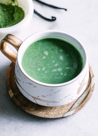 a green vanilla matcha latte inside a white and gold ceramic mug on a white table