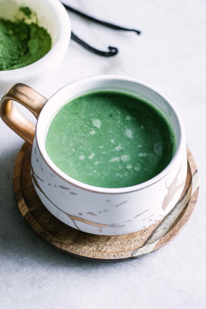 a green vanilla matcha latte inside a white and gold ceramic mug on a white table