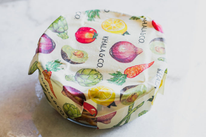 a glass food container covered with beeswax paper on a white table