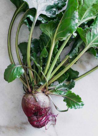 a red beet with beet greens on a white table