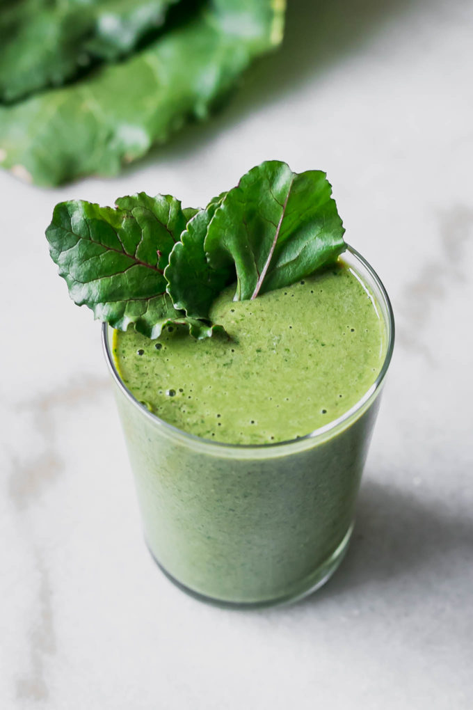 a green smoothie with beet greens garnish on a white table