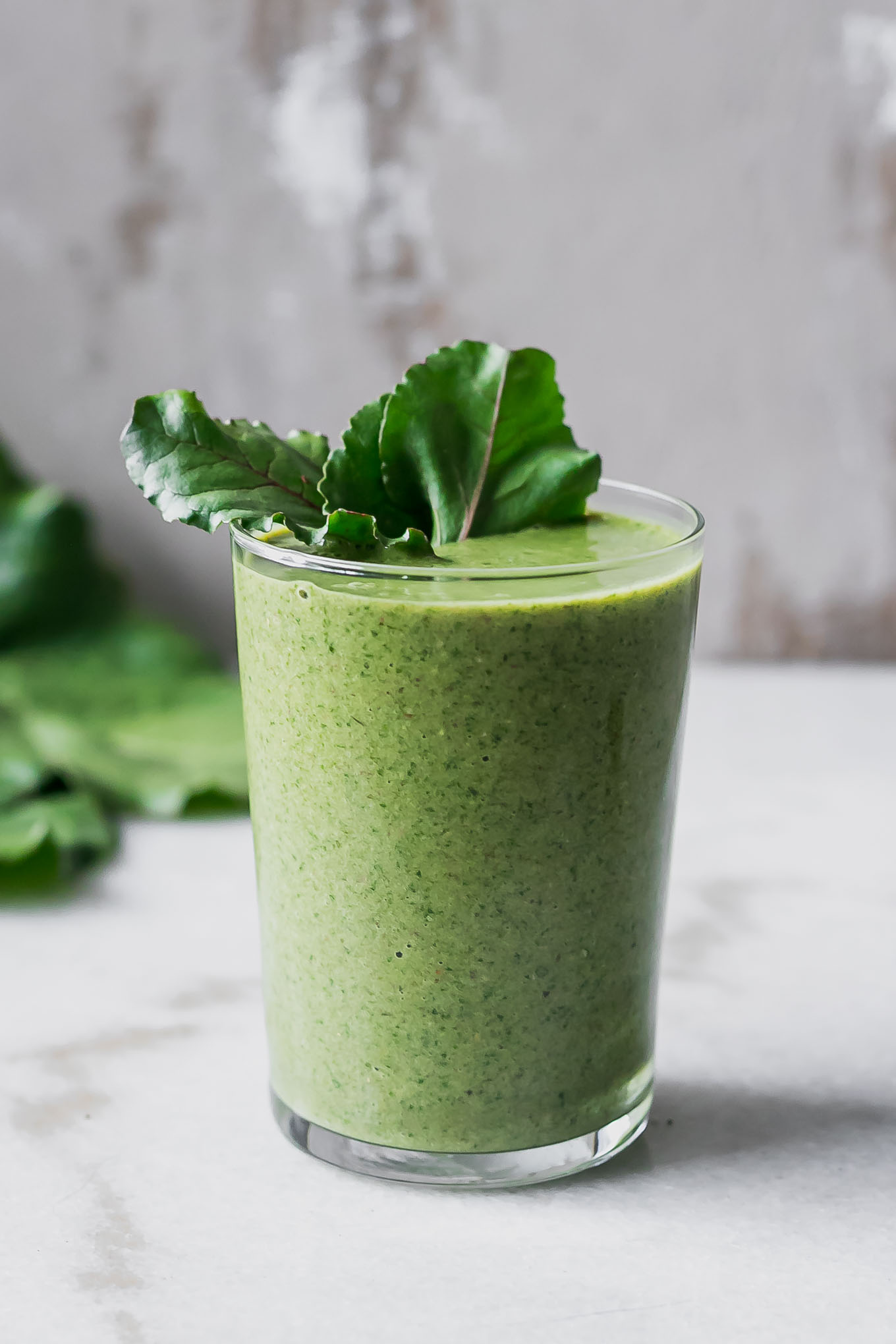 a green beet tops smoothie in a glass on a white table with a beet in the background