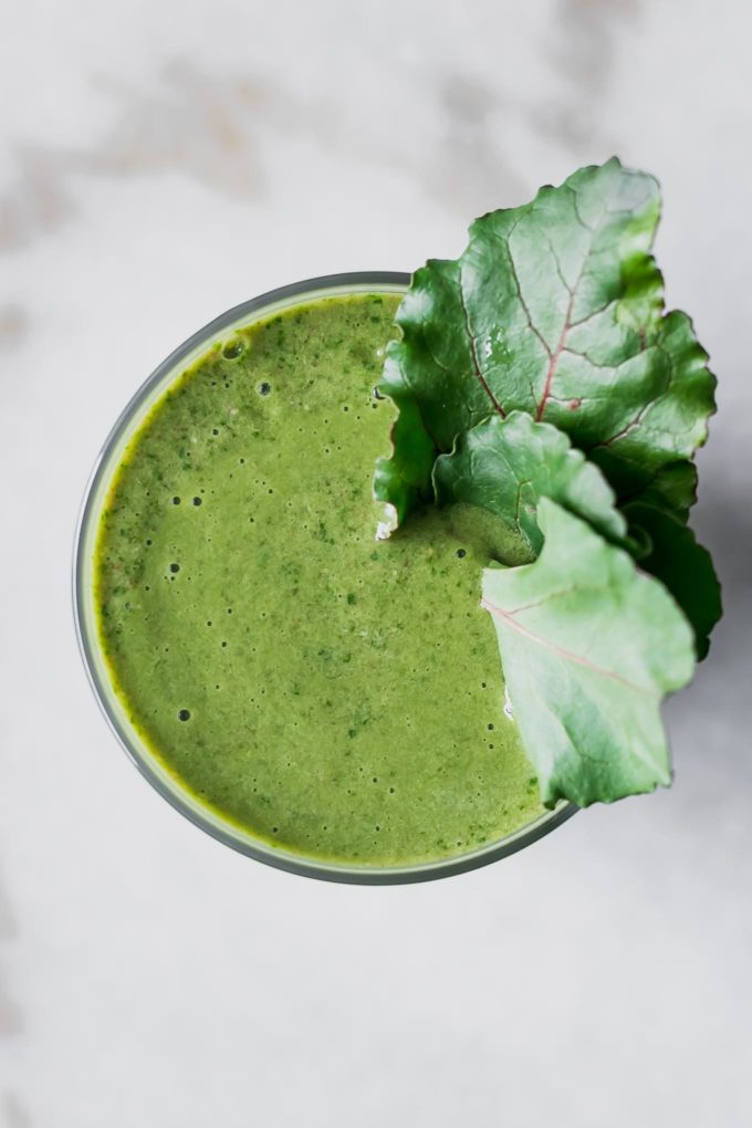 a photo of the top of a green smoothie with three beet leaves as a garnish