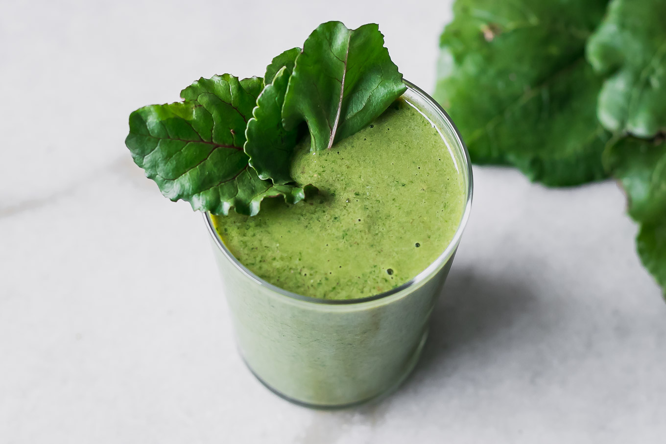 a green beet leaves smoothie in a glass on a white table