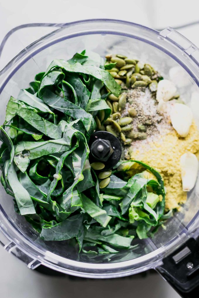 ingredients for pesto with brussels sprouts tops in a food processor on a white table