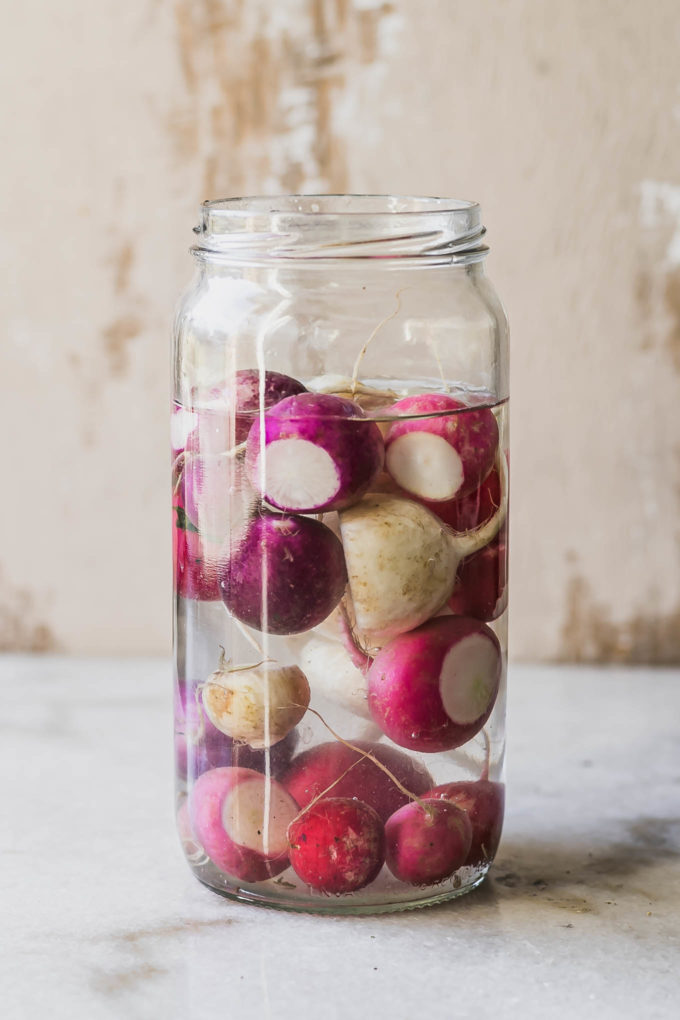 radishes in a jar with water on a white table