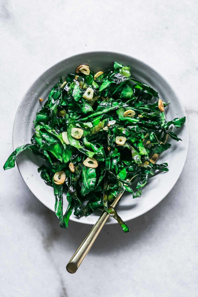 pan fried brussels sprouts leaves in a white bowl with a gold for on a white table