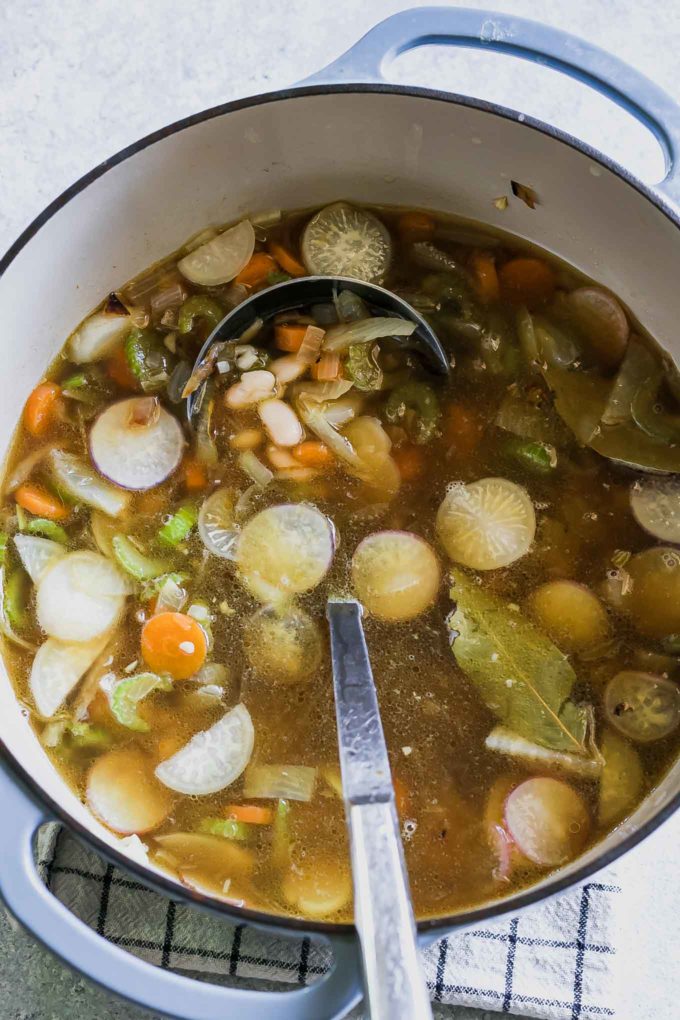 vegetable soup broth in a dutch oven pot with a metal ladel