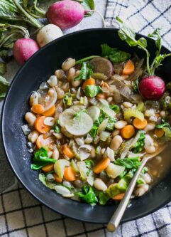 vegetable soup with radish greens in a black bowl on a blue table