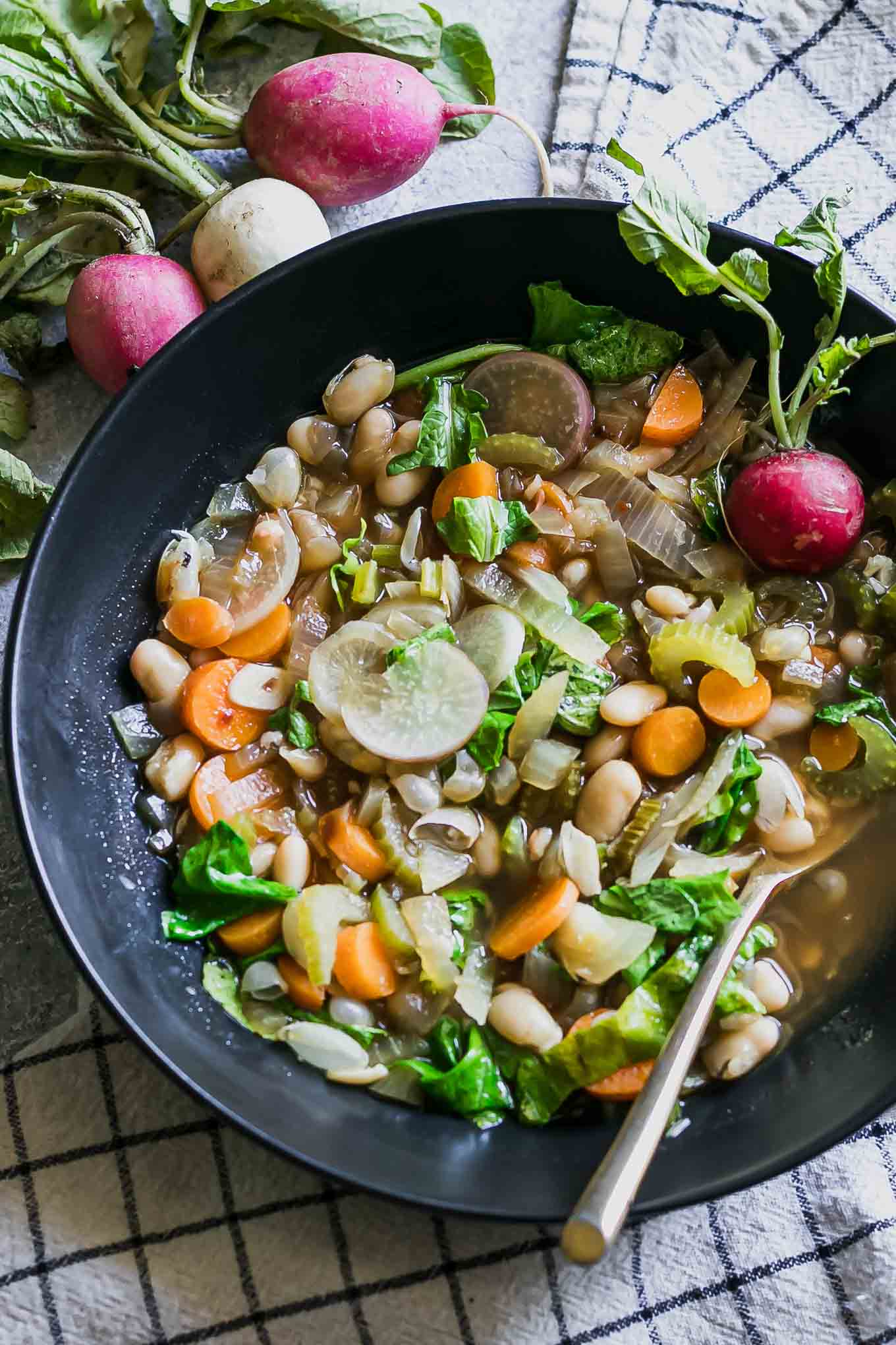 vegetable soup with radish greens in a black bowl on a blue table