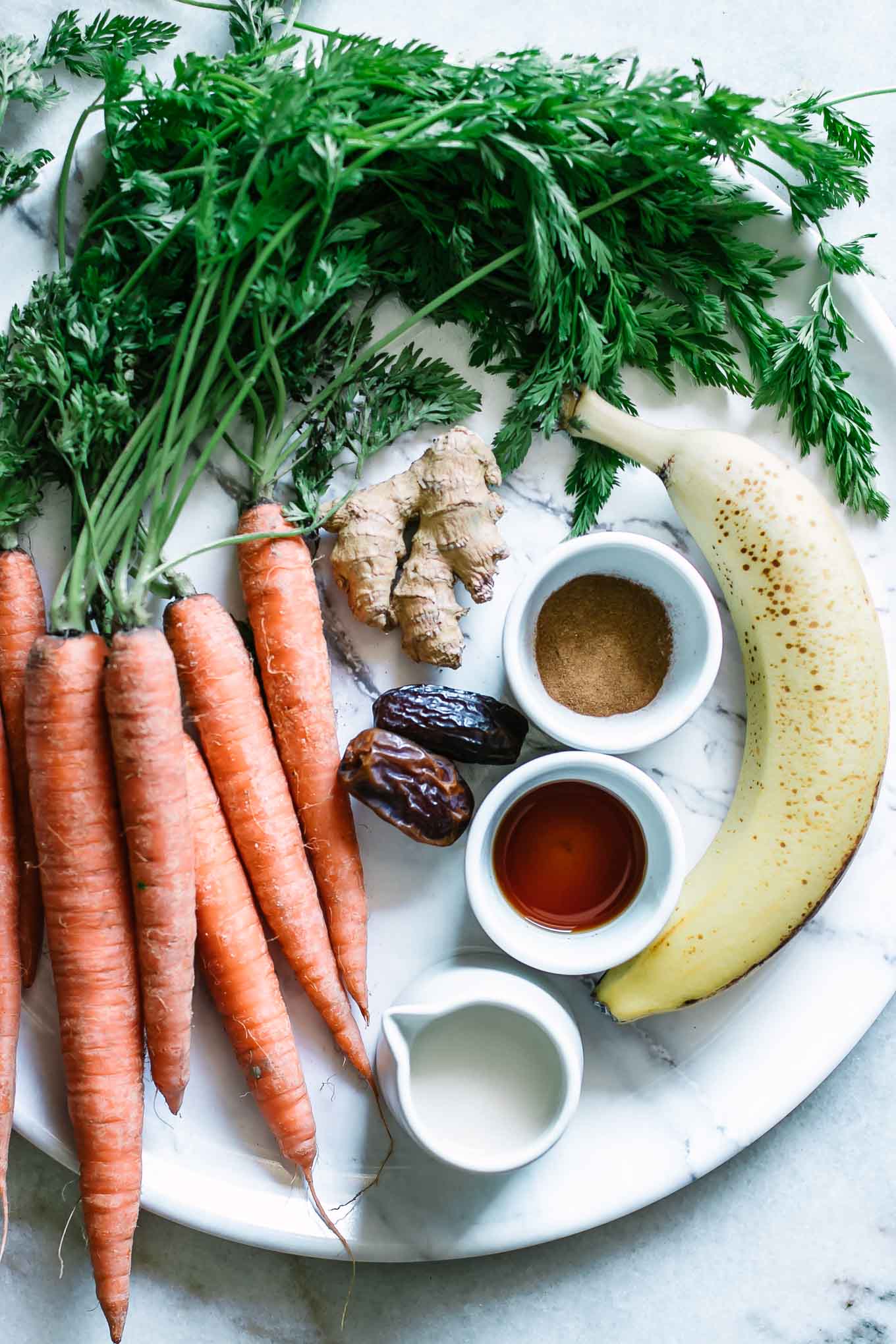 carrots, banana, ginger, dates, and bowls of spices on a white table