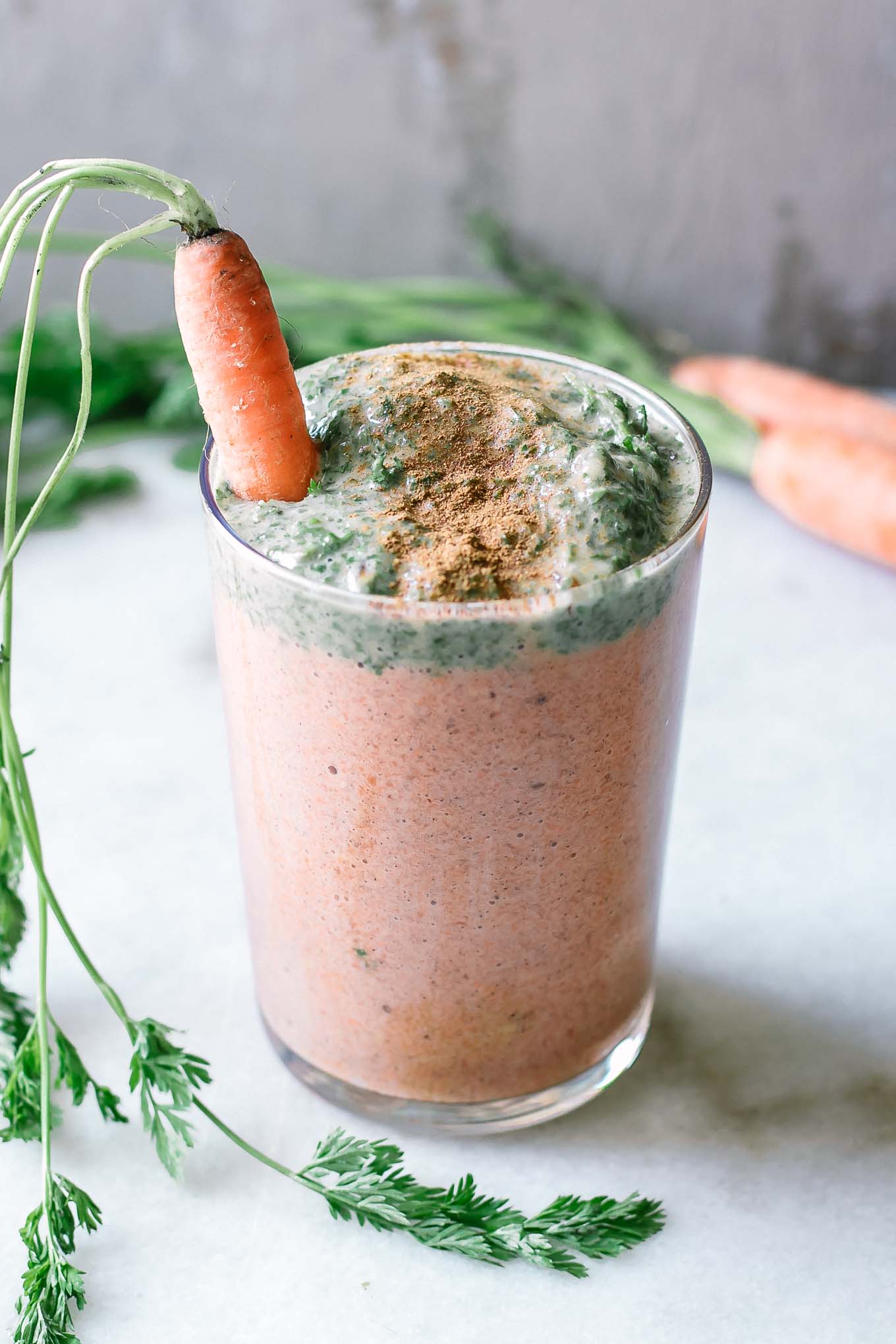 an orange carrot smoothie with green carrot greens as garnish on a white table