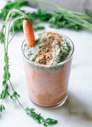 an orange and green carrot smoothie with carrot greens garnished with a carrot with green leaves