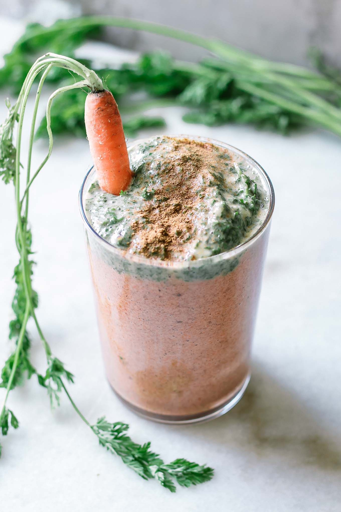 an orange and green carrot smoothie with carrot greens garnished with a carrot with green leaves