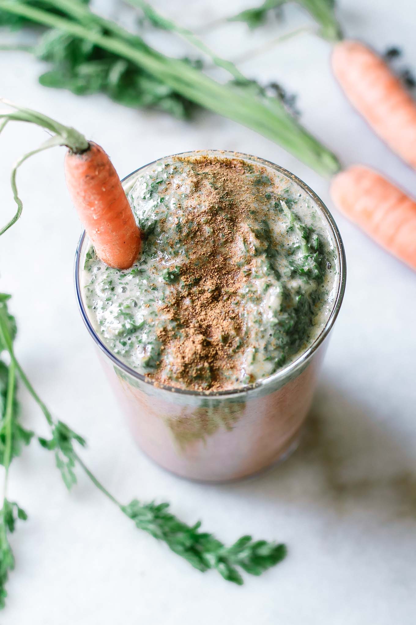 an orange and green carrot top smoothie in a glass with a carrot garnish and sprinkled cinnamon