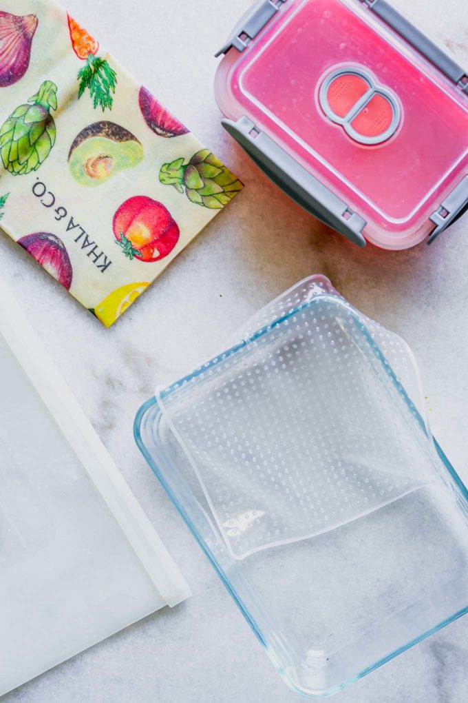 glass food storage jars, beeswax wrap, silicone bags, and other sustainable food storage alternatives to plastic bags on a white table