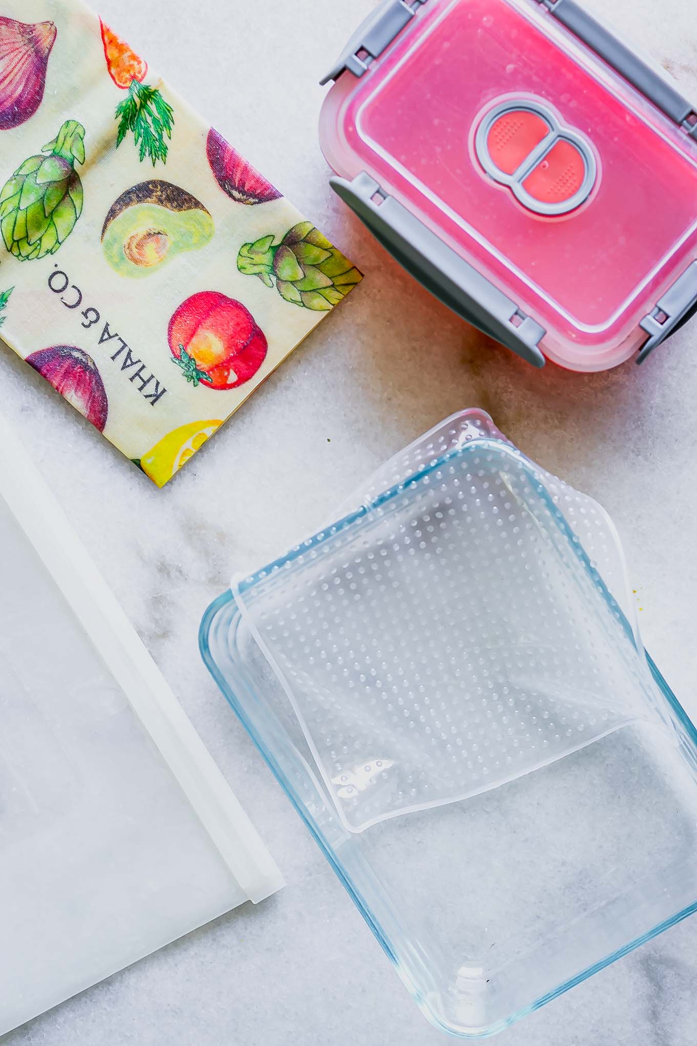glass food storage jars, beeswax wrap, silicone bags, and other sustainable food storage alternatives to plastic bags on a white table