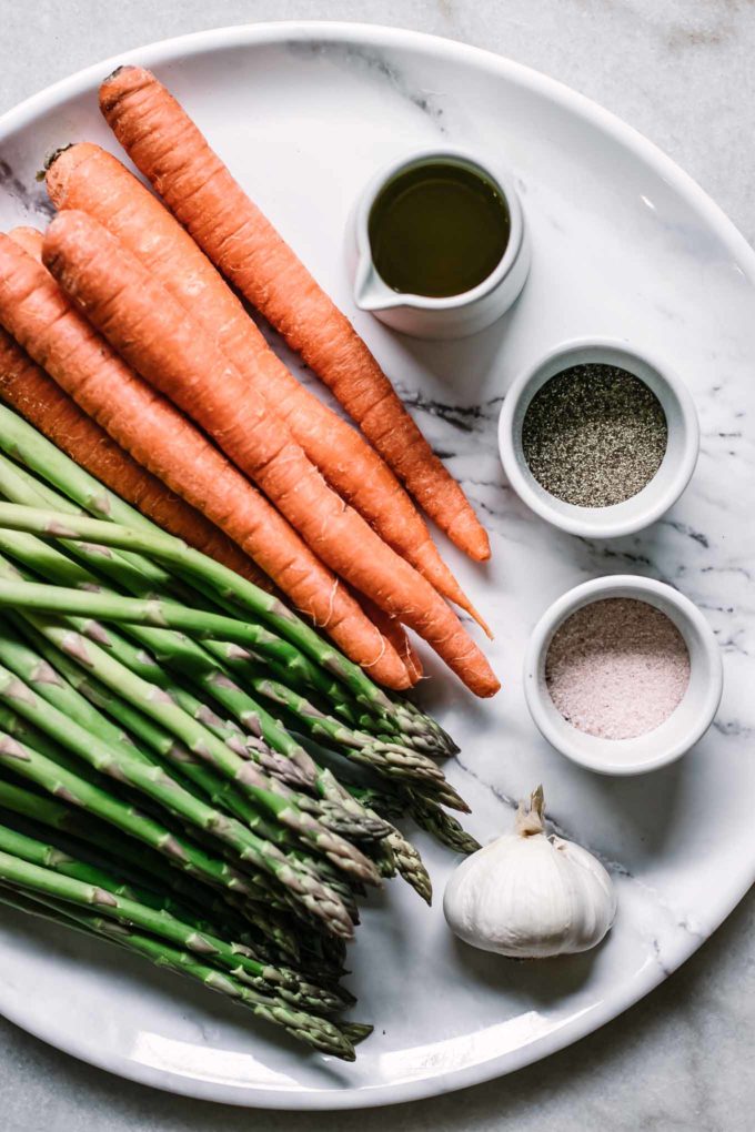 carrots, asparagus, garlic, and bowls of oil, salt, and pepper on a white table