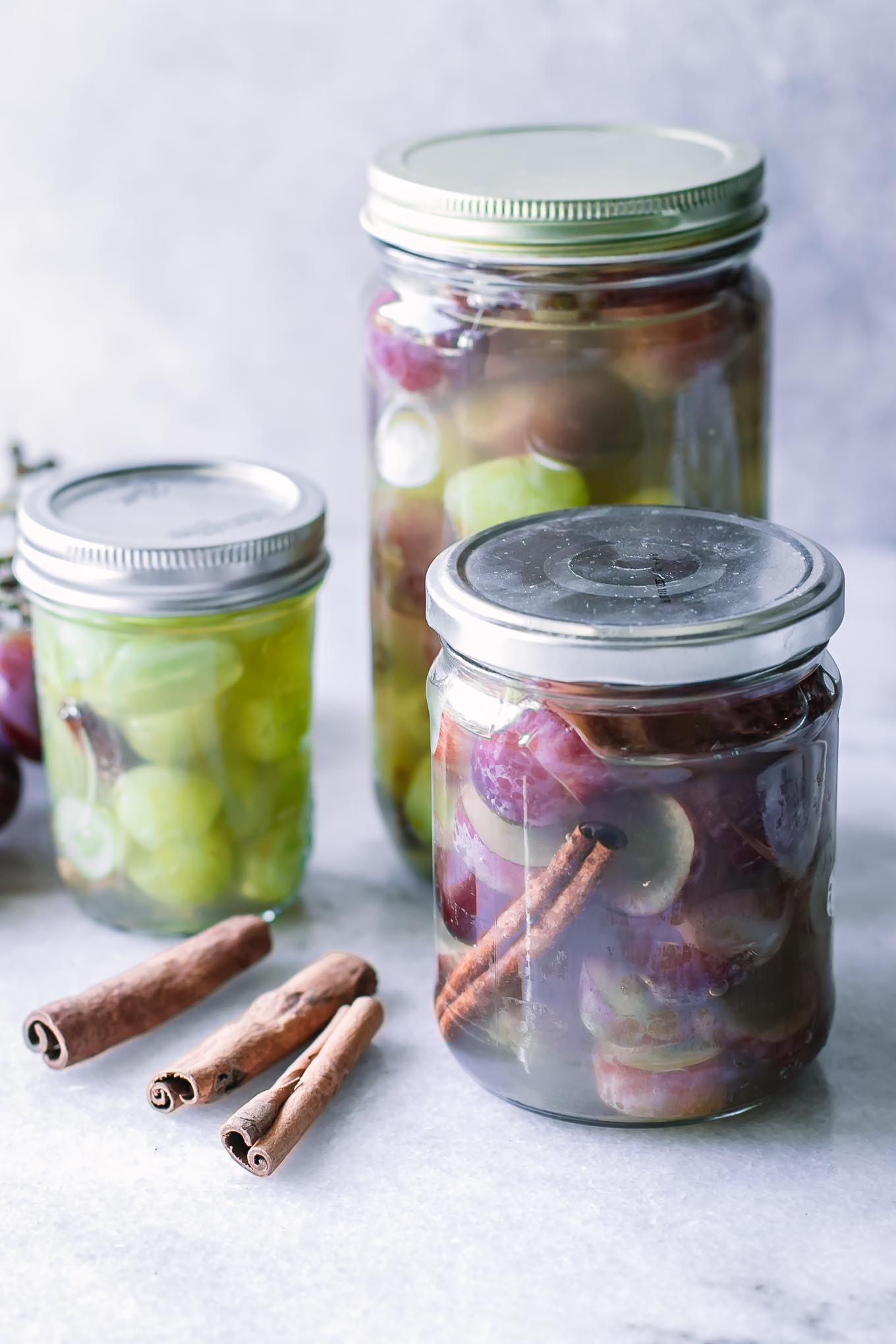 jars of green and red grapes in pickling jars on a white table
