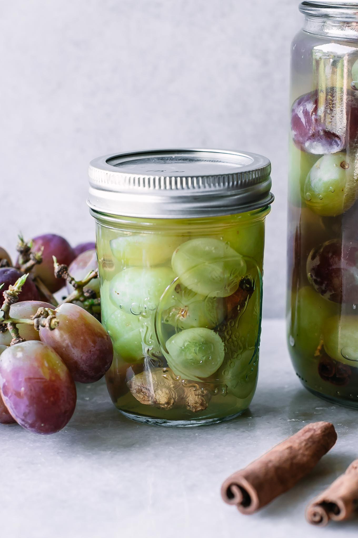 a jar of sliced green grapes in a pickling jar with a bunch of whole red grapes