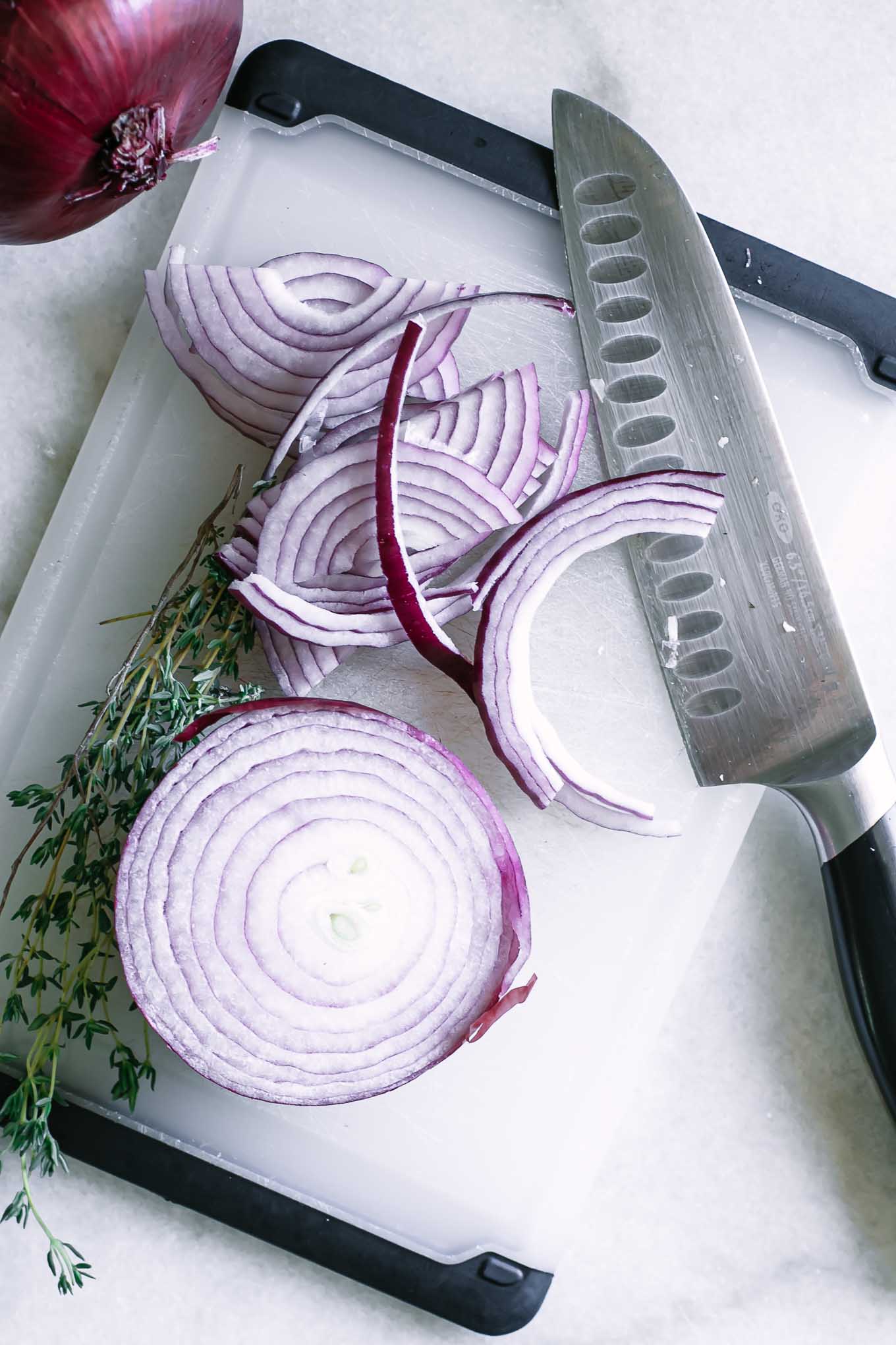 a cutting board with a knife and slices of red onions