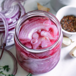 overhead view of pickled red onions in a jar on a plate with herbs and spices