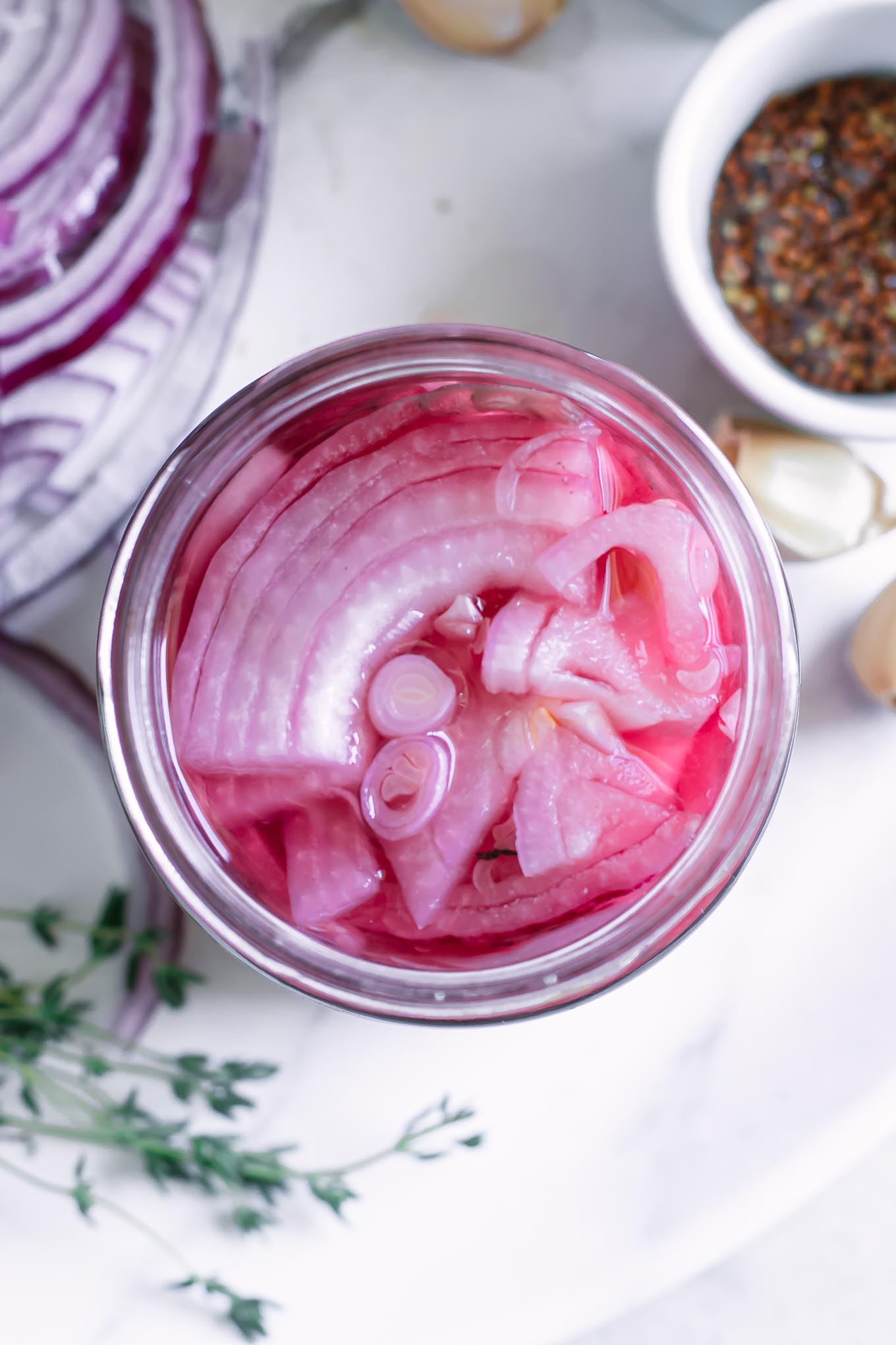 overhead view of pickled red onions in a jar on a counter with herbs and spices