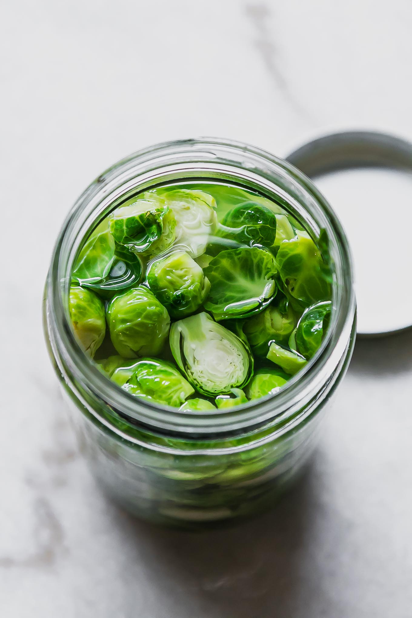 brussels sprouts in a pickling brine in a glass jar on a white table