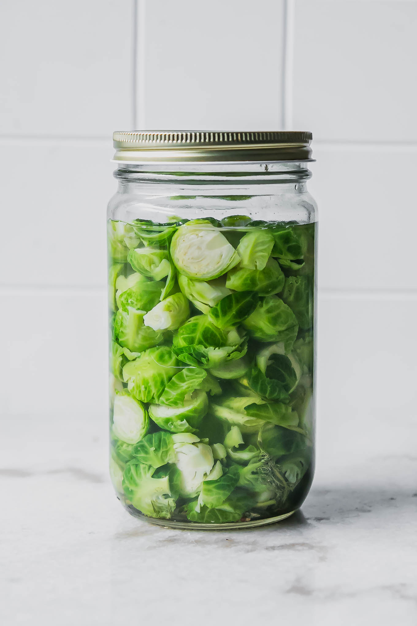 pickled brussels sprouts in a jar on a white table