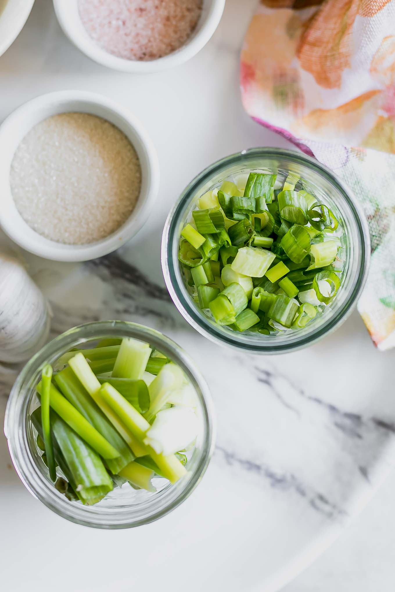 a jar of sliced green onions, and a jar of cut green onions on a white table