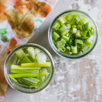 two jars of pickled scallions on a wood table