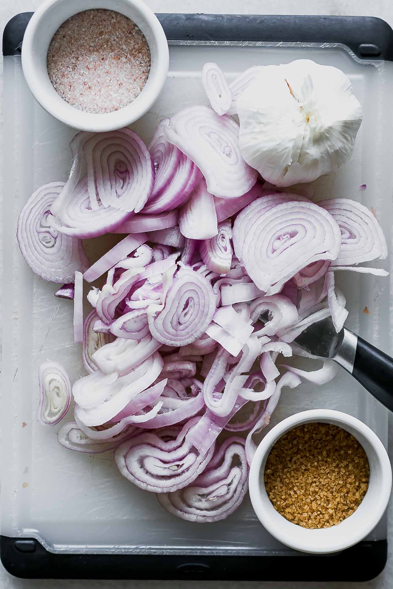 sliced shallots for pickling on a cutting board with a knife and garlic