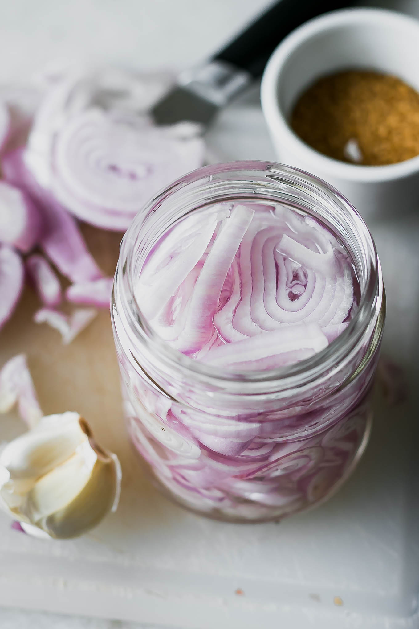sliced shallots in pickling brine in a jar on a white table