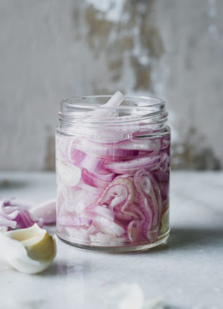 sliced shallots in a jar with pickling brine on a white countertop