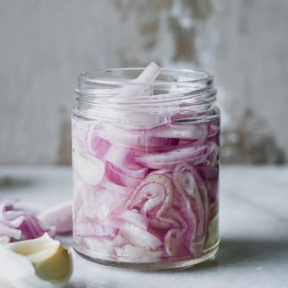 sliced shallots in a jar with pickling brine on a white countertop