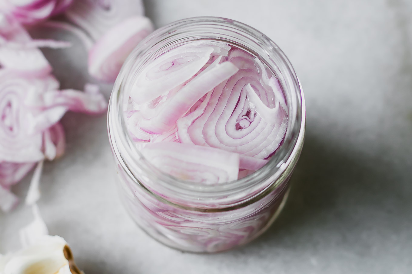 sliced shallots in a pickling jar on a white table