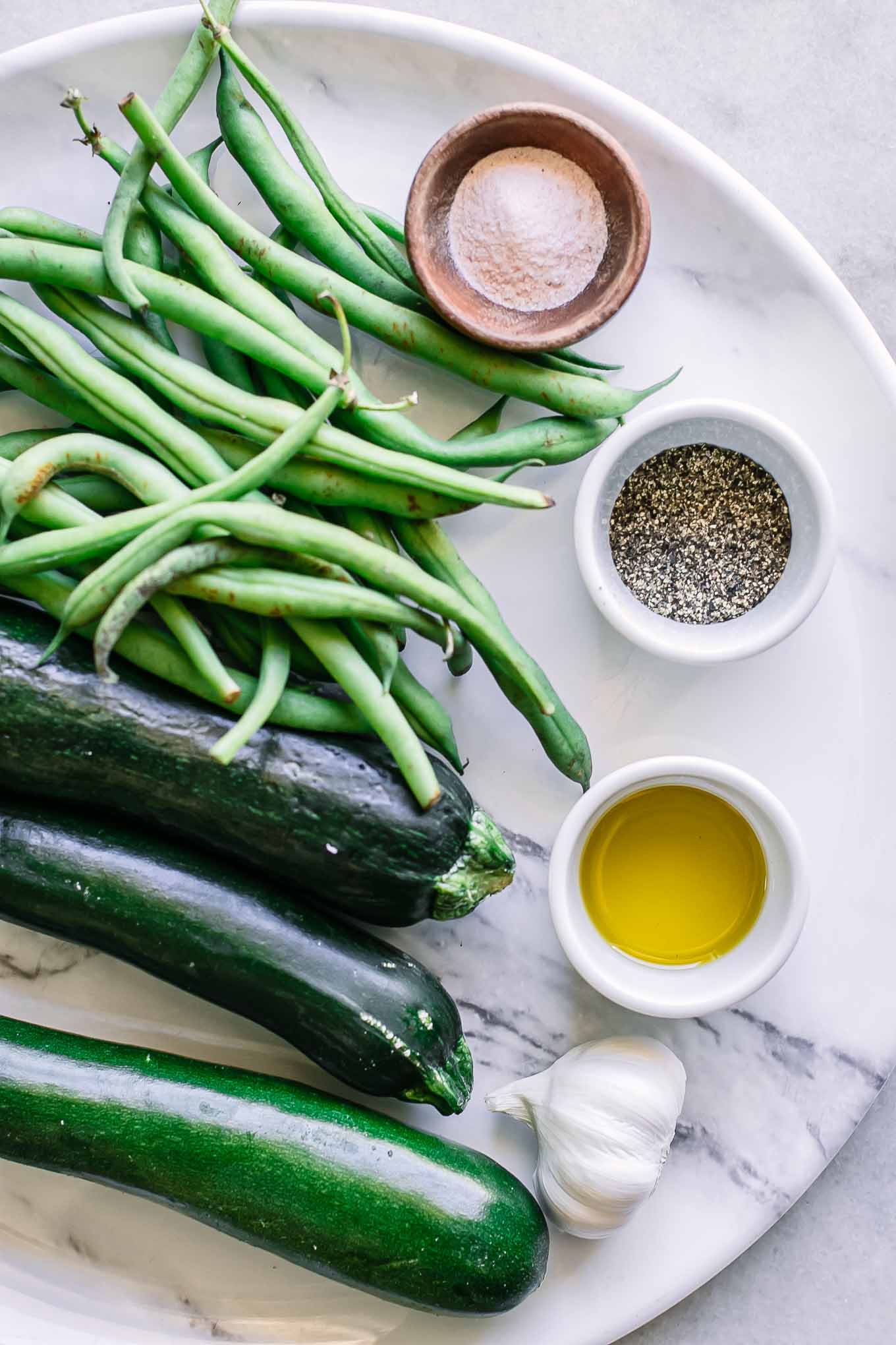 fresh green beans and zucchini on a table with bowls of olive oil, salt, and pepper