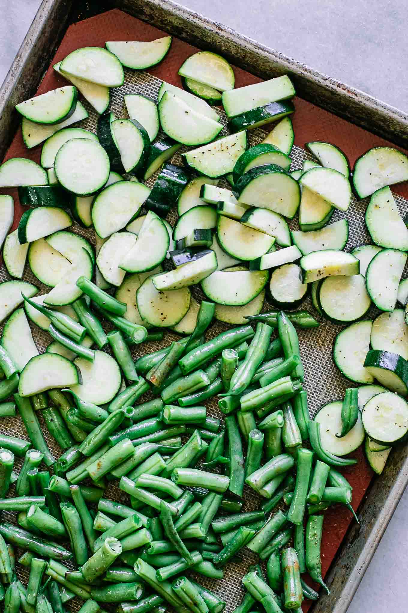 a roasting pan with zucchini and green beans on a white table