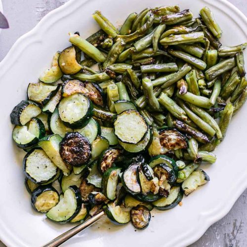 a white side dish with baked zucchini and green beans on a countertop