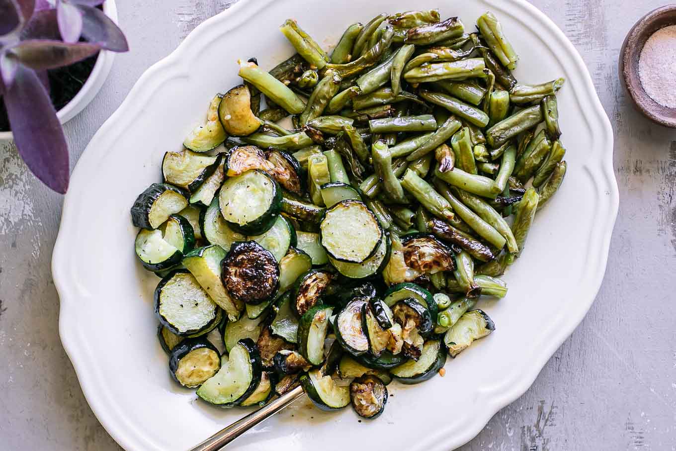a white side dish with baked zucchini and green beans on a countertop