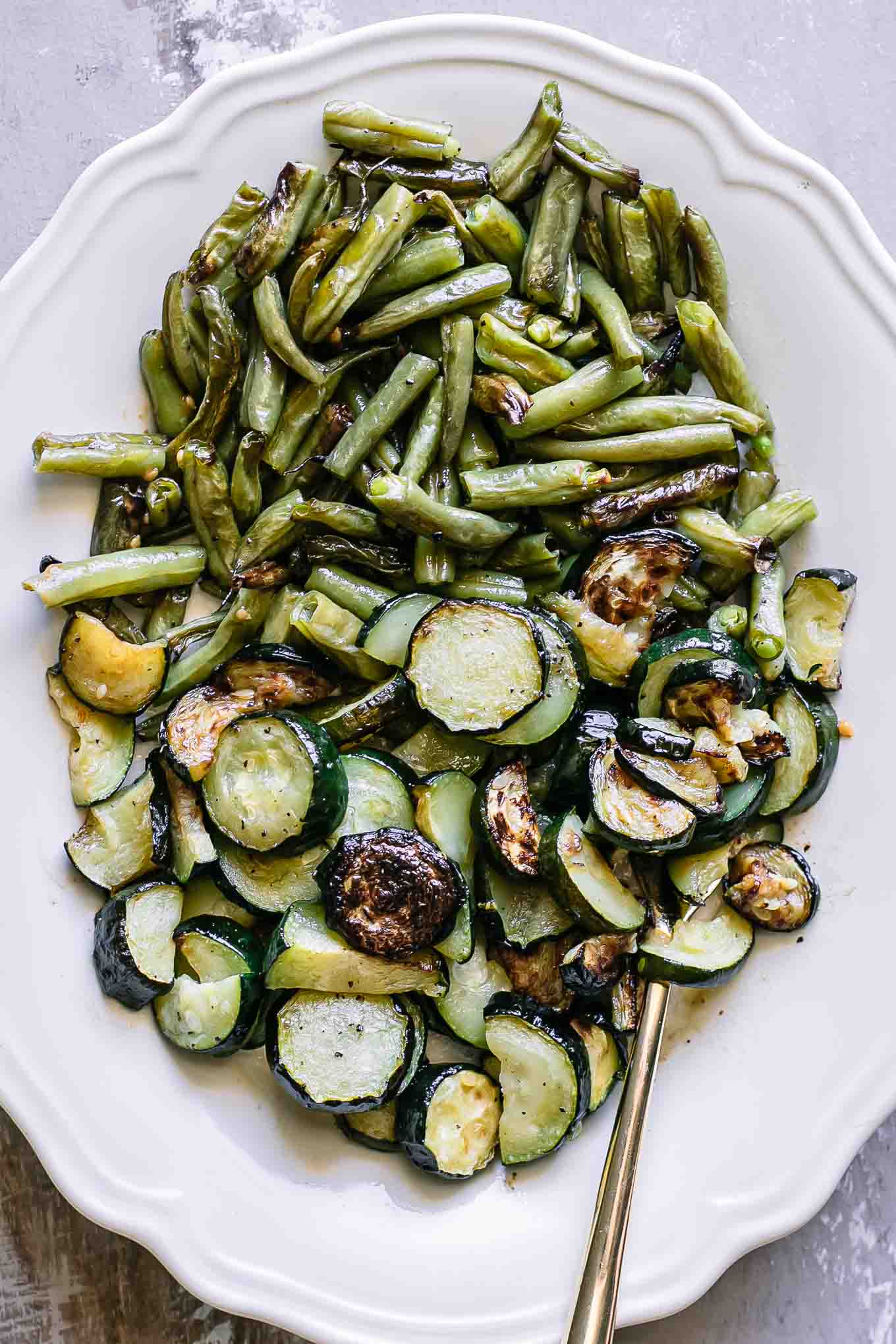 a white plate with baked green beans and zucchini on a white table