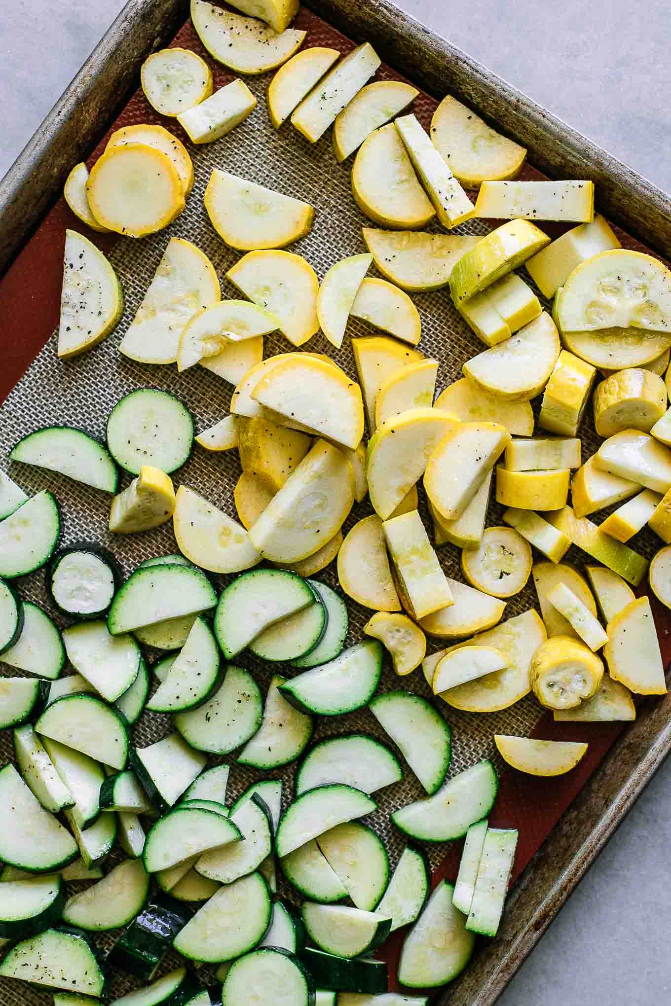 sliced yellow squash and zucchini on a roasting pan before baking