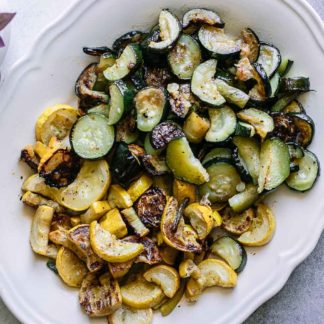 a white side dish of roasted zucchini and squash on a blue table