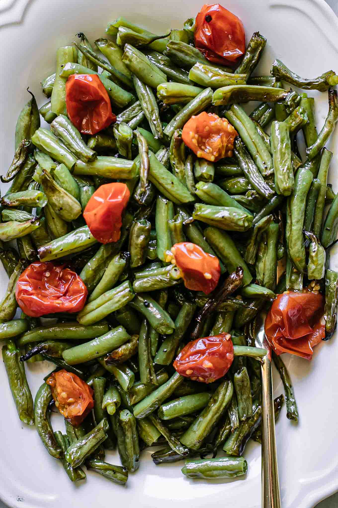 a white plate with baked green beans and cherry tomatoes