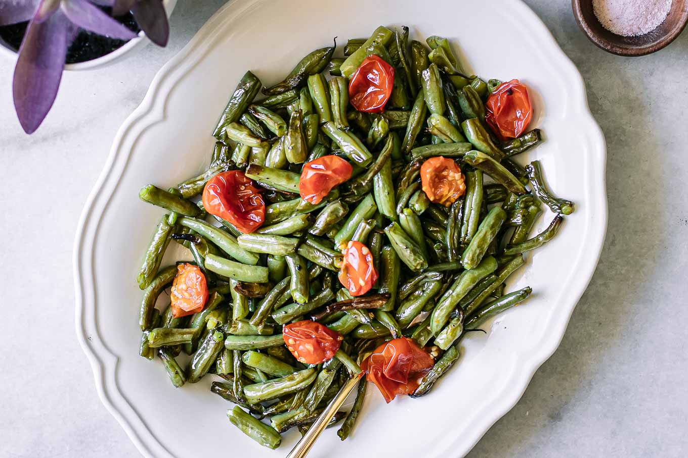 roasted tomatoes and green beans on a white plate on a white table