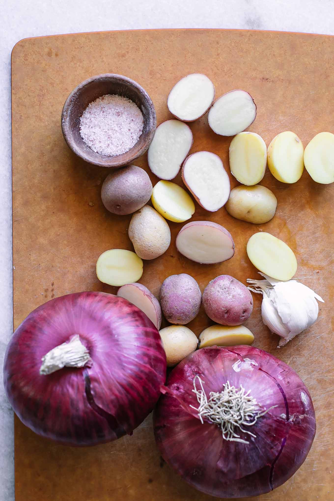 sliced potatoes and red onions on a wood cutting board