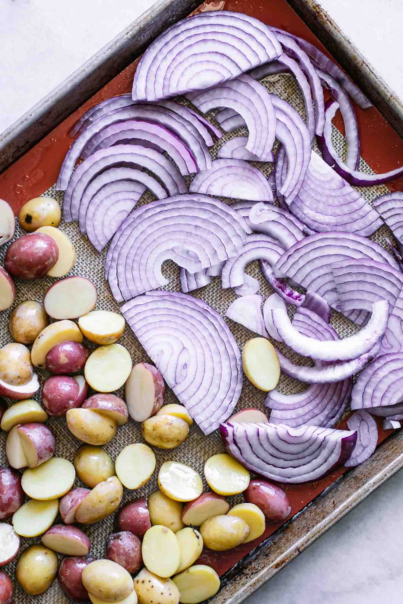 sliced potatoes and onions on a roasting pan before baking