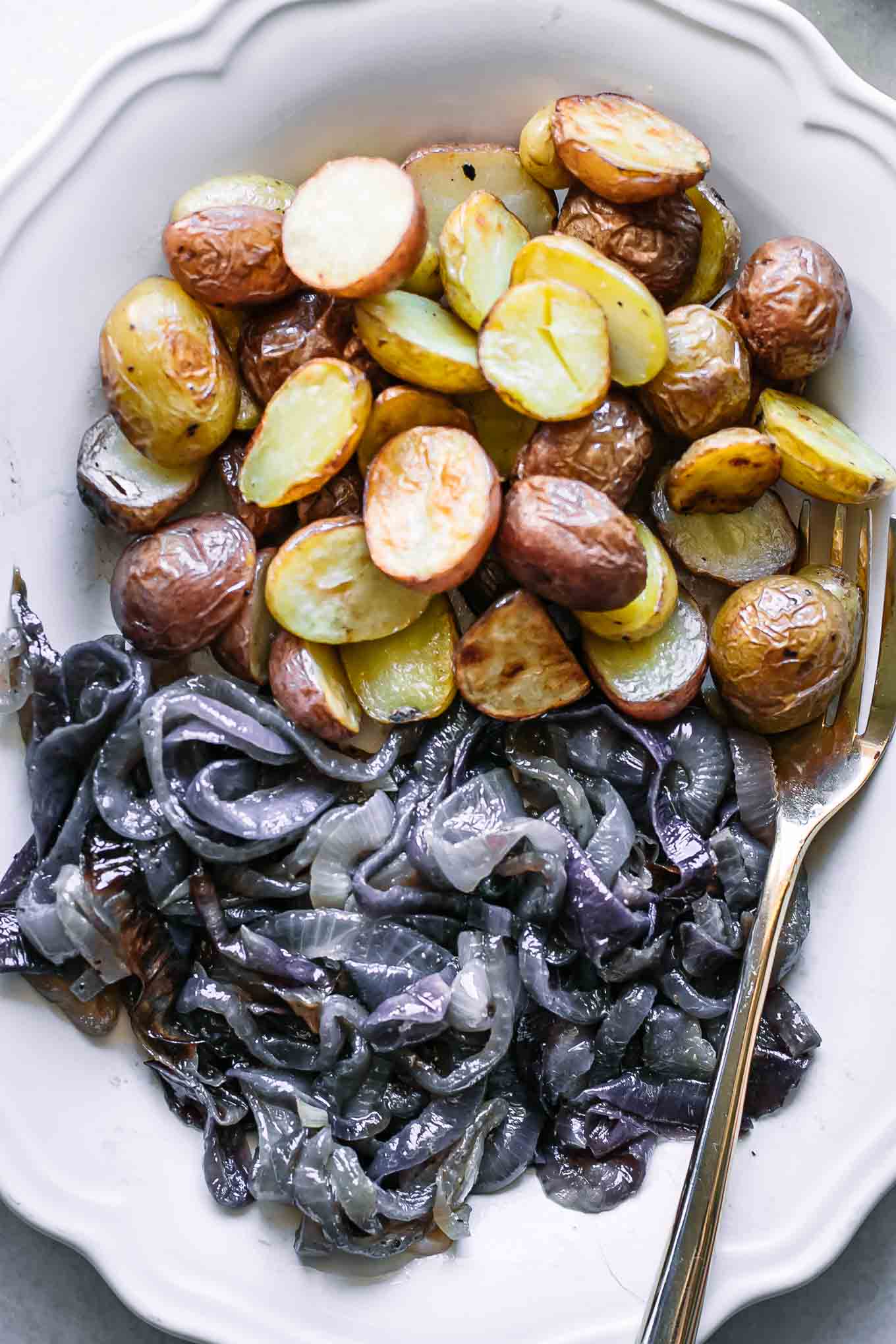 a close up of roasted potato and onions on a white plate