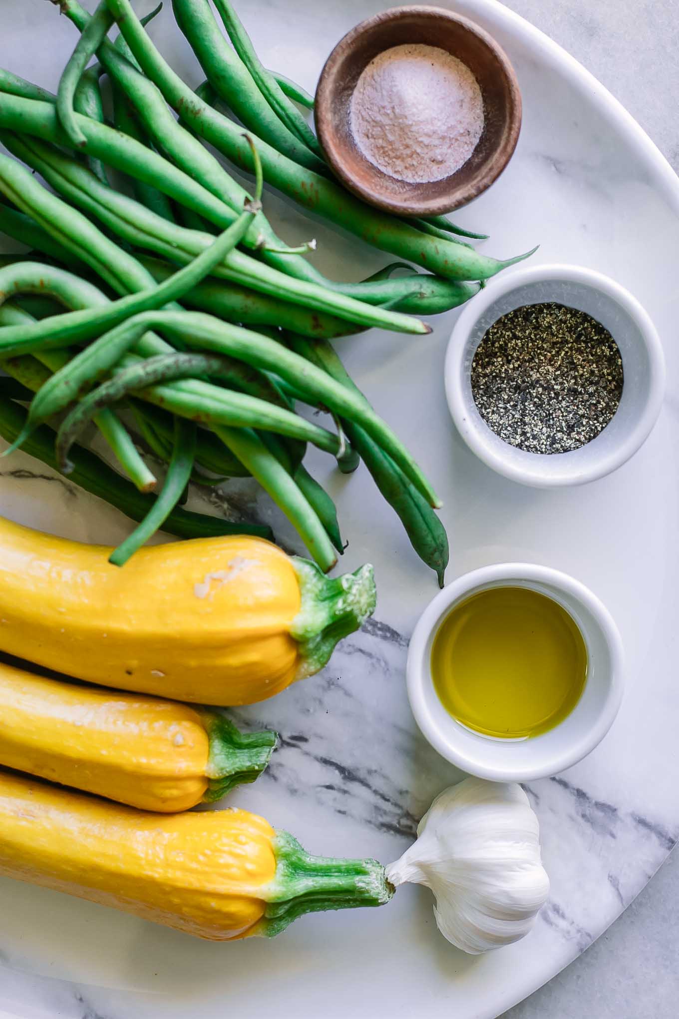 summer squash, green beans, and bowl of olive oil, salt, and pepper on a white table