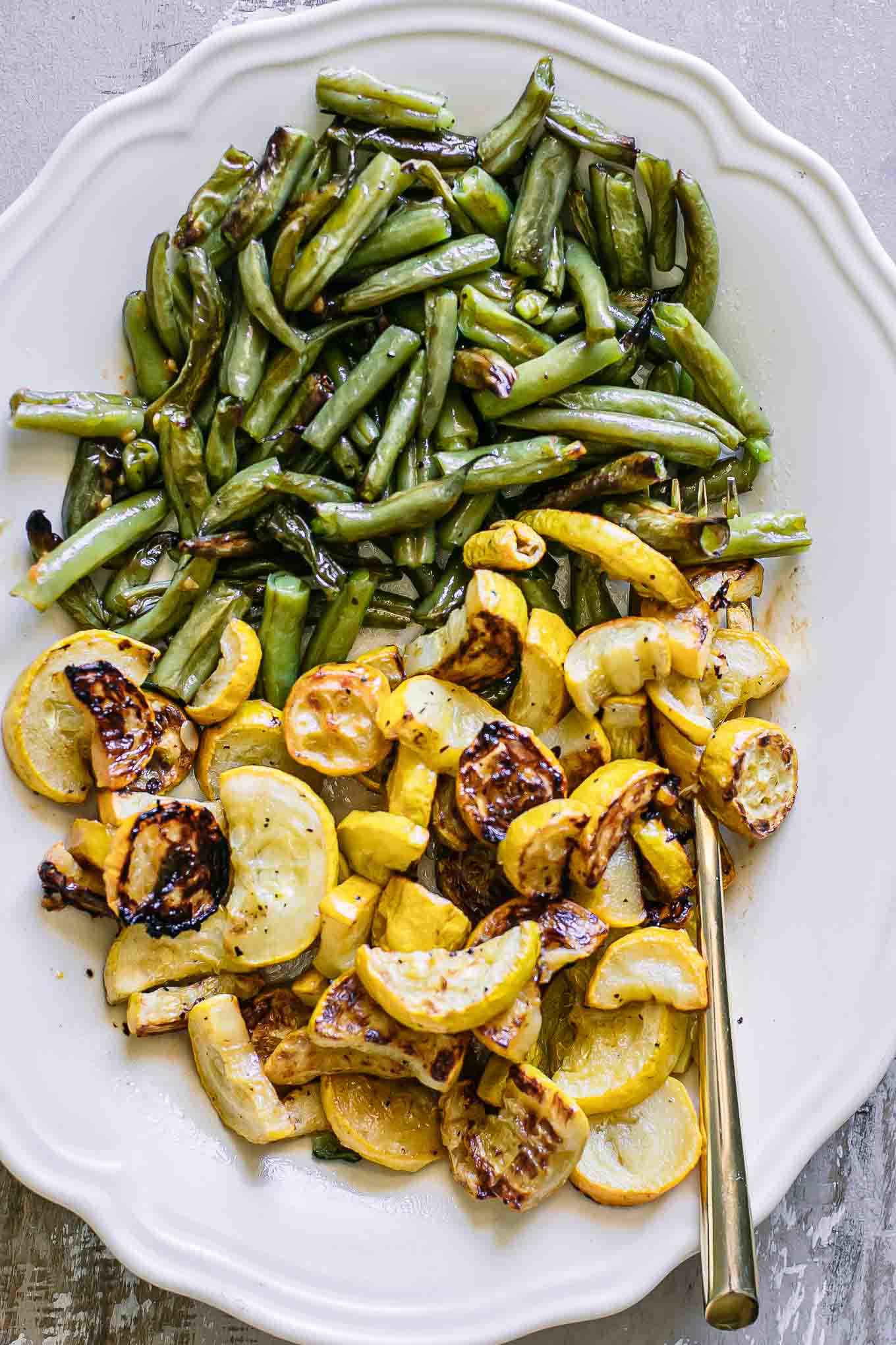 baked green beans and squash side dish with a gold fork on a white table